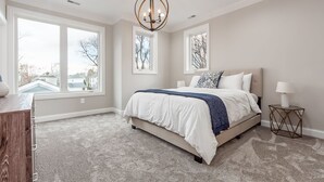 A bedroom with a large bed, a chandelier, and multiple windows.
