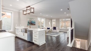A spacious kitchen with a central island, large windows, and a modern chandelier.