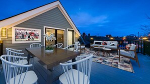 A covered patio with a dining table and chairs, a sofa, and a view of the cityscape at dusk.