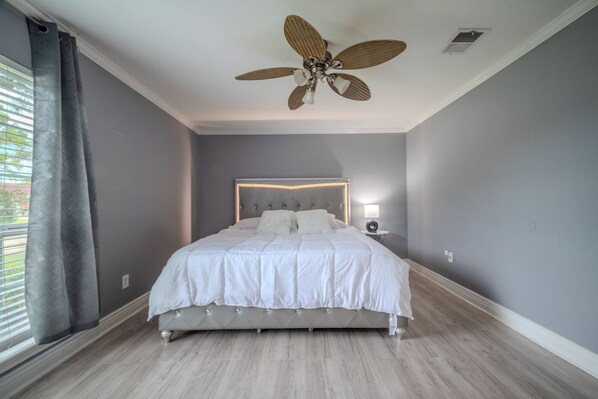 A bedroom with a bed, a ceiling fan, a bedside table with a lamp, and a window with curtains. - Spacious 4-bedroom house in awesome Houston (Houston)