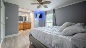 A bedroom with a large bed, a ceiling fan, a TV mounted on the wall, and a bathroom visible in the background. - Spacious 4-bedroom house in awesome Houston (Houston)
