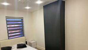 A bedroom with a bed, a nightstand, a window with blinds, and a dark accent wall. - Seaside Escape in Blackpool (Blackpool)