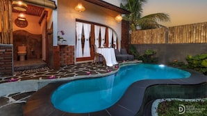 Una zona de piscina con diseño curvo, un espacio de descanso con mesa y sillas, y una valla de madera.