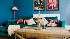 Ein Zimmer mit einem petrolfarbenen Sofa, einem Holztisch und zwei gerahmten Kunstwerken an der Wand.