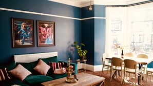 Ein Wohnzimmer mit einem grünen Sofa, einem Holztisch und einem Essbereich mit weißem Tisch und Stühlen.