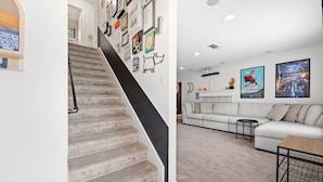 A staircase with a black handrail leading to a living area with a white sofa and a coffee table. - The Quirky Casita in League City (League City)