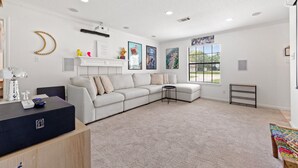 A modern living room with a sectional sofa, a small round table, and a fireplace. There are framed pictures on the wall and a window with blinds. - The Quirky Casita in League City (League City)