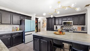 A modern kitchen with dark cabinetry, a central island, a blue refrigerator, and a chandelier. - The Quirky Casita in League City (League City)