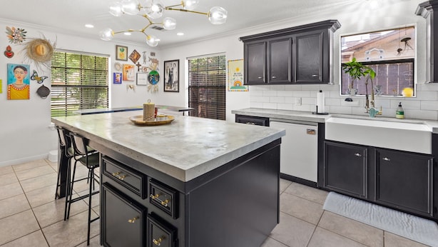 A modern kitchen with dark cabinetry, a central island, and a chandelier. - The Quirky Casita in League City (League City)