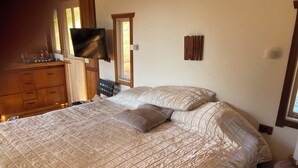 A bedroom with a bed, wooden dresser, and a flat-screen TV mounted on the wall.