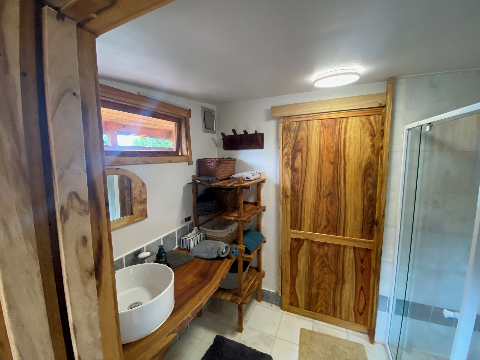 A bathroom with a wooden vanity, a white sink, a towel rack, and a wooden door.