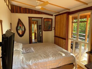 A bedroom with a bed, a ceiling fan, a mirror, and a wooden door leading to a balcony.