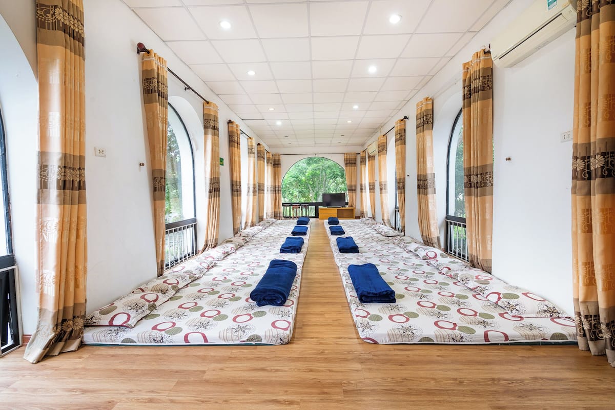 Una habitación con una hilera larga de camas centradas, cada una con una toalla azul y ropa de cama estampada.