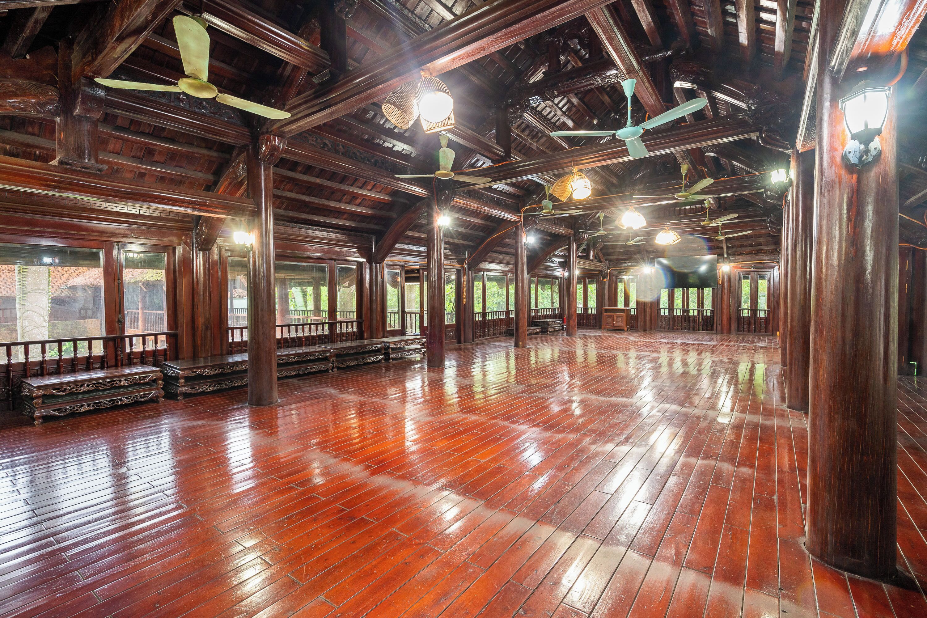 A spacious hall with wooden floors and columns, large windows, and ceiling fans.