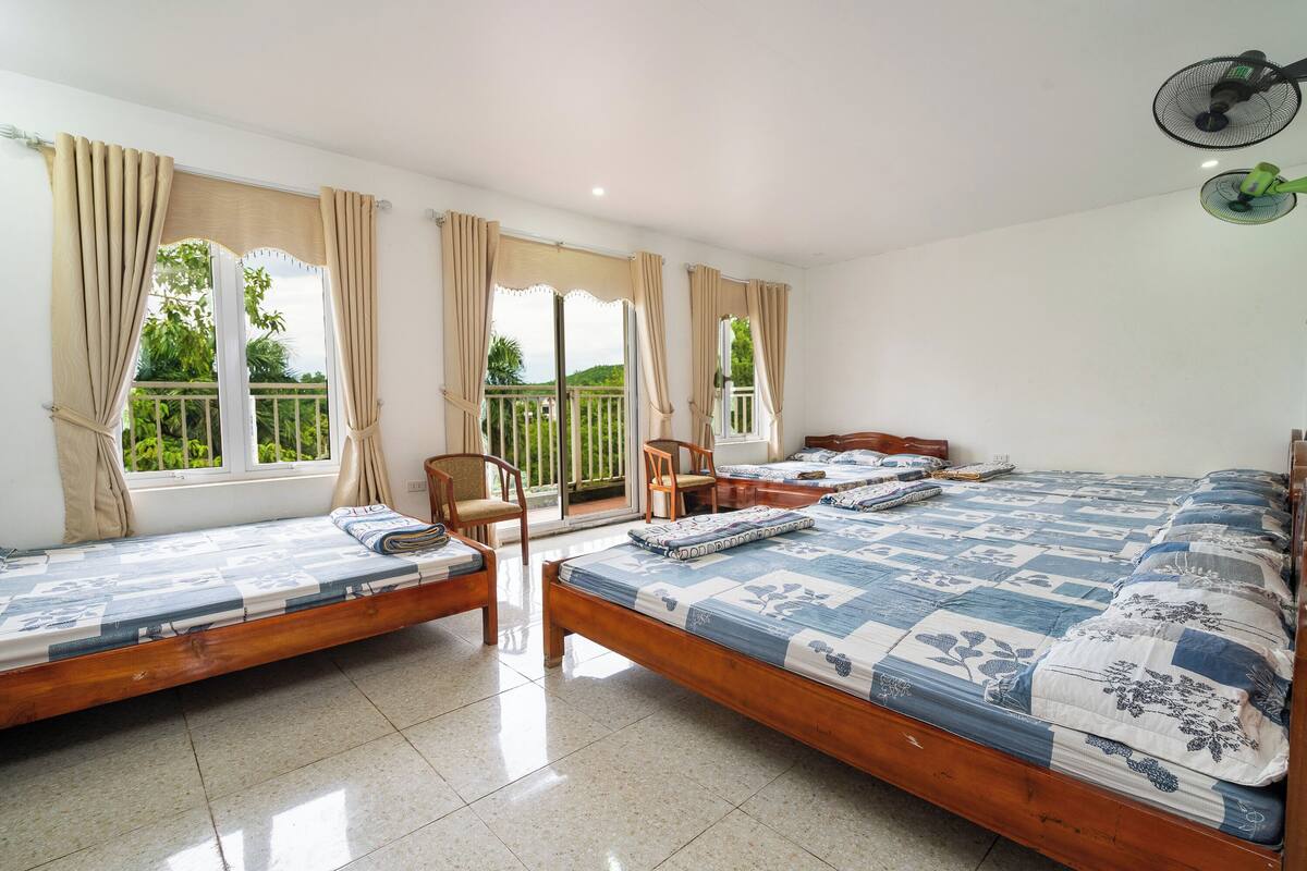 Una habitación con dos camas individuales, una mesita, sillas y un balcón con vistas a zonas verdes.