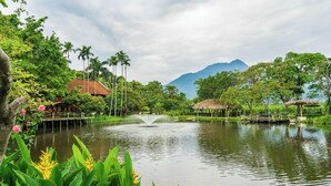 A serene lakeside view with a fountain, lush greenery, and a mountain in the background.