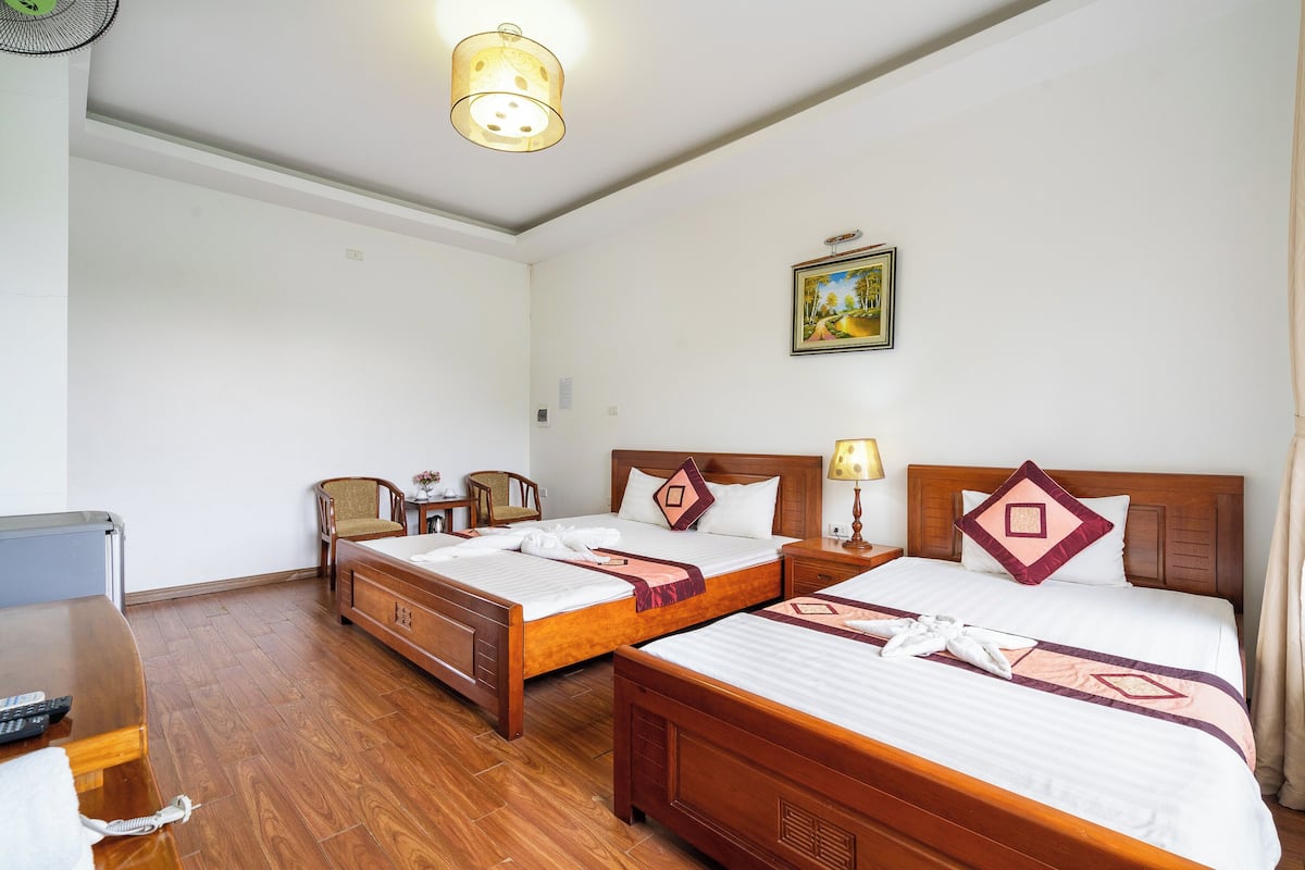 Habitación de hotel con dos camas de madera, un escritorio, una silla, una lámpara y un cuadro en la pared.