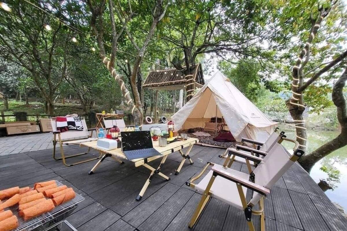 Un espacio al aire libre para acampar con una tienda de campaña, una mesa con una computadora portátil y una parrilla con comida.