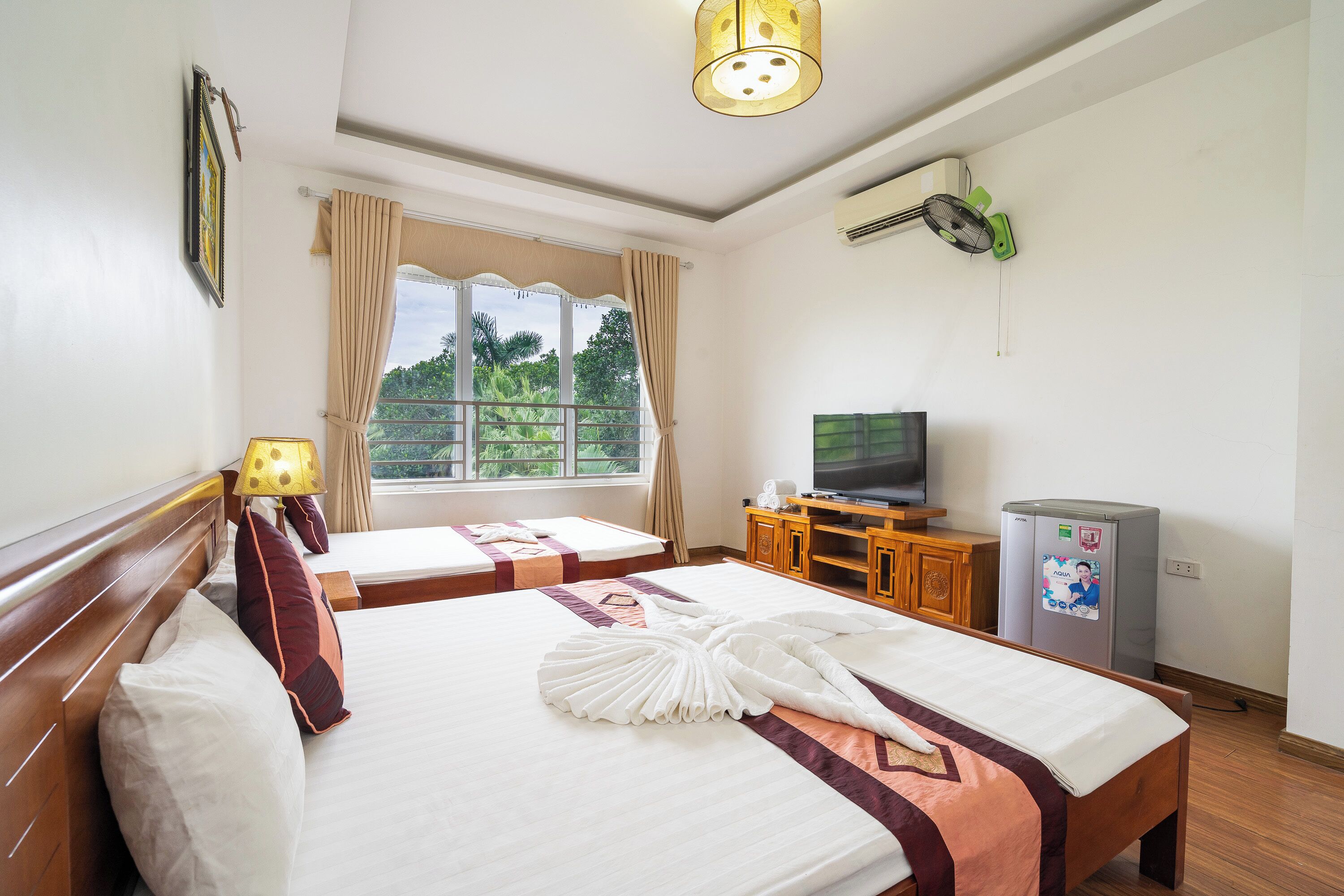 A hotel room with two beds, a television, a refrigerator, and a window with curtains.