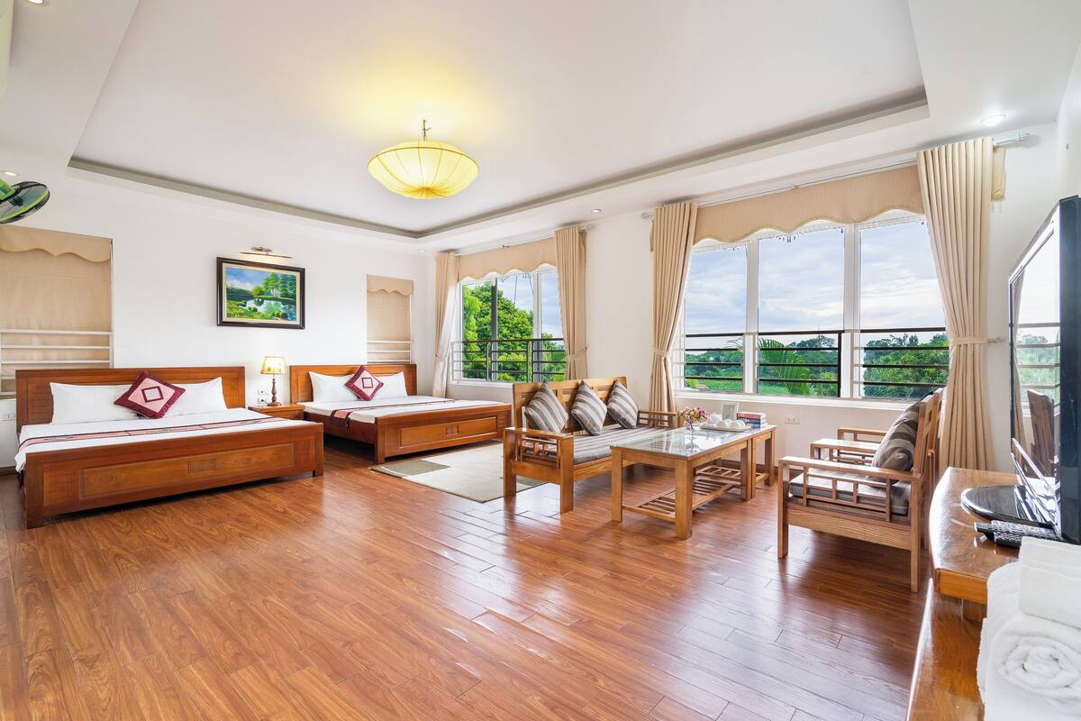 Una habitación amplia con piso de madera, una cama grande, un sofá, una mesita y un televisor.