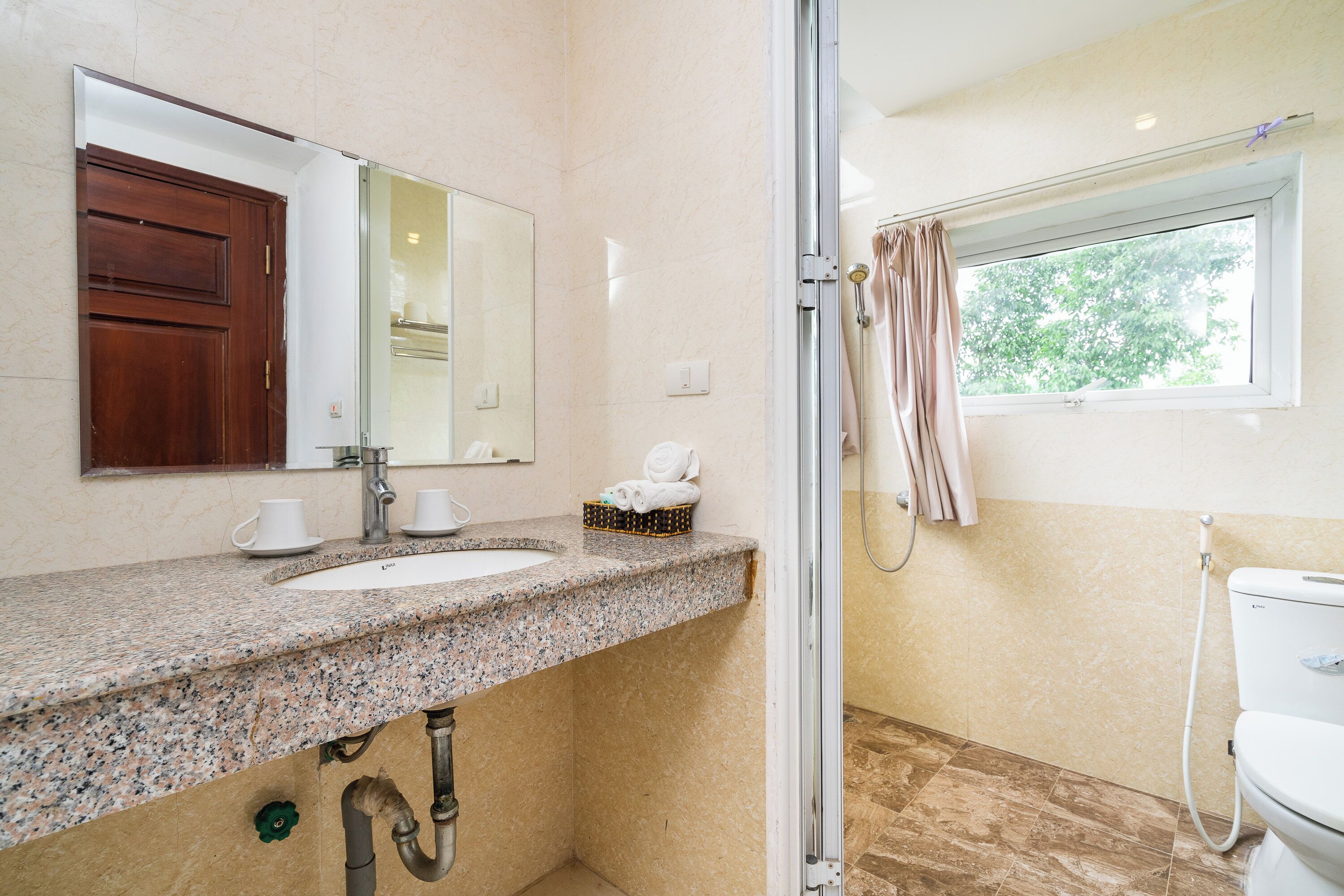 Un baño con lavamanos de encimera de granito, espejo, toallero y ventana con cortina de ducha.
