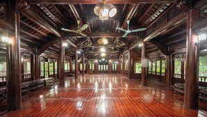 A spacious hall with wooden floors and columns, large windows, and ceiling fans.