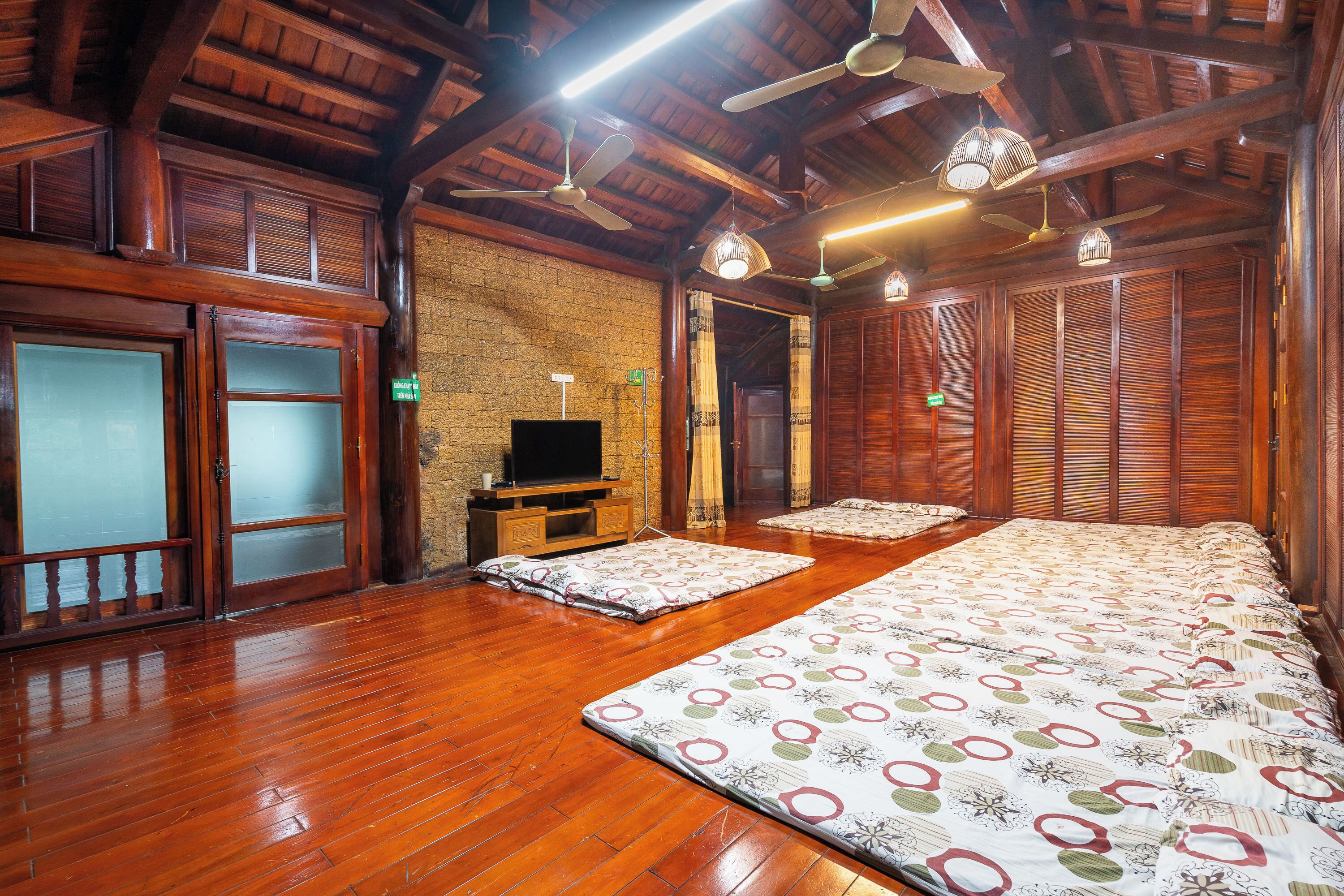Amplia habitación con piso de madera, una cama grande, televisor y ventilador de techo.