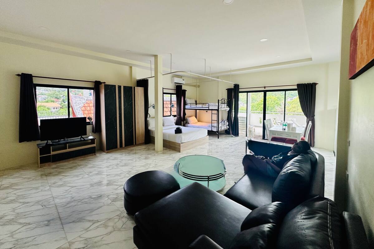 A modern living room with a flat-screen TV, a sofa, a coffee table, and a balcony with a view of the city.