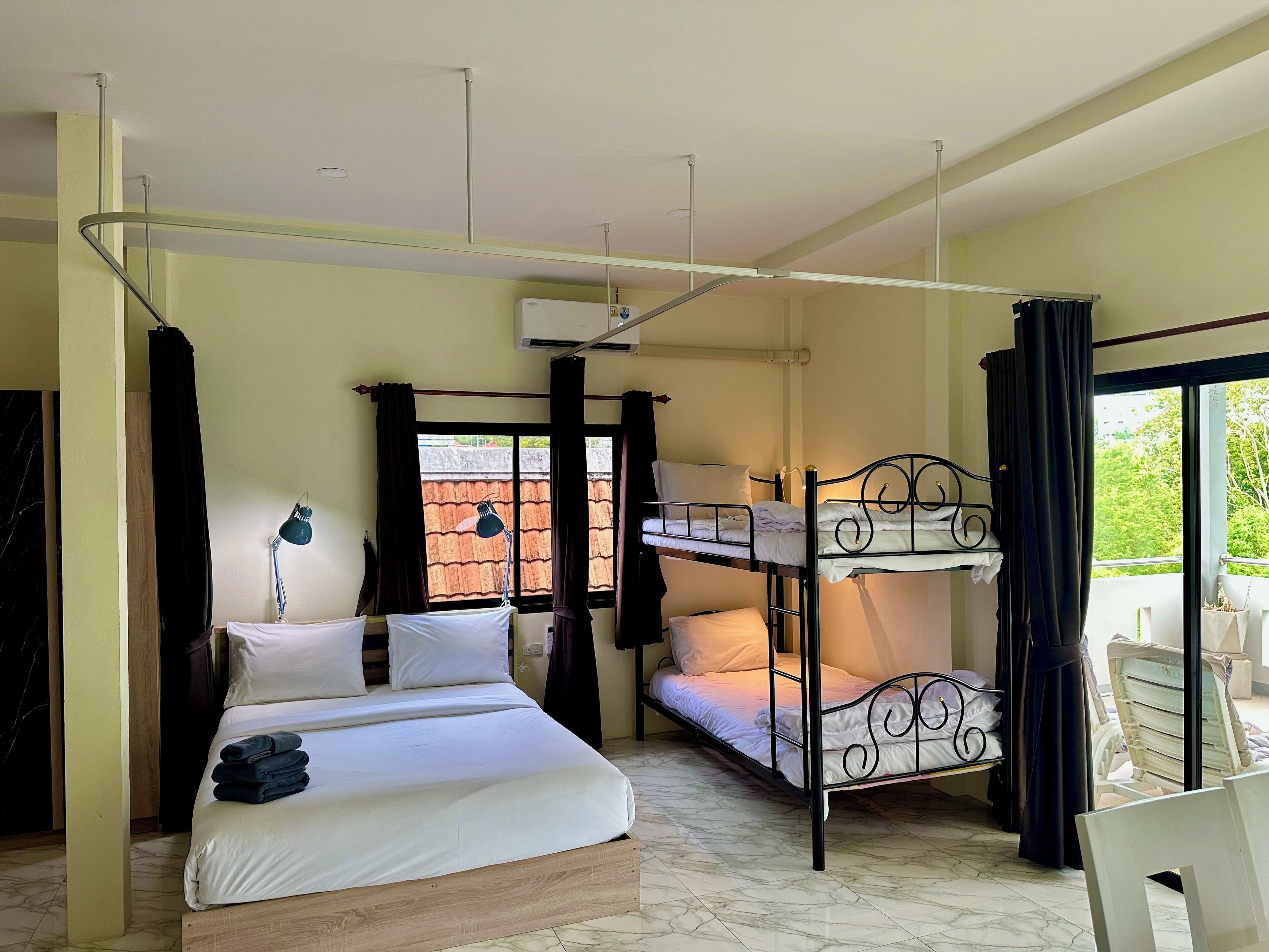 A room with a bed, a bunk bed, a desk, a chair, a lamp, and a window.