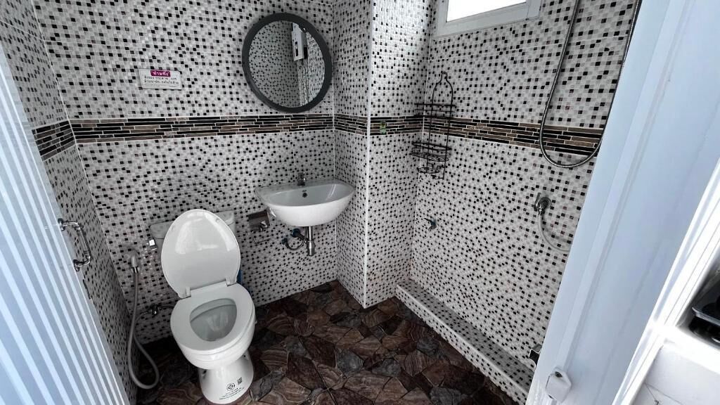 Un baño con inodoro, lavabo y zona de ducha, con paredes de azulejos estampados y suelo de losa.
