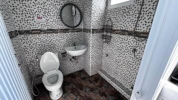 Un baño con inodoro, lavabo y zona de ducha, con paredes de azulejos estampados y suelo de losa.