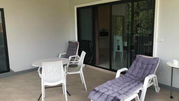 A balcony with a table, two chairs, and a single sun lounger.