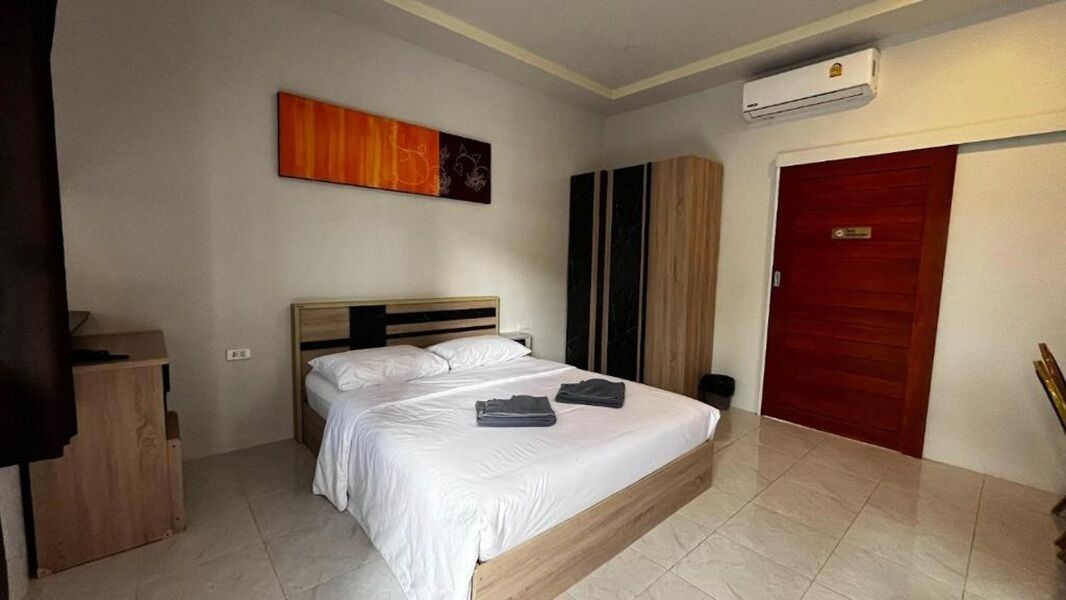 A bedroom with a bed, a wardrobe, a red door, and an air conditioning unit.