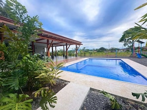 Una piscina con zona cubierta y plantas tropicales.
