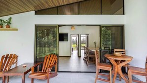 A modern interior with a wooden dining table and chairs, large glass doors leading to an outdoor area, and a flat-screen TV mounted on the wall.