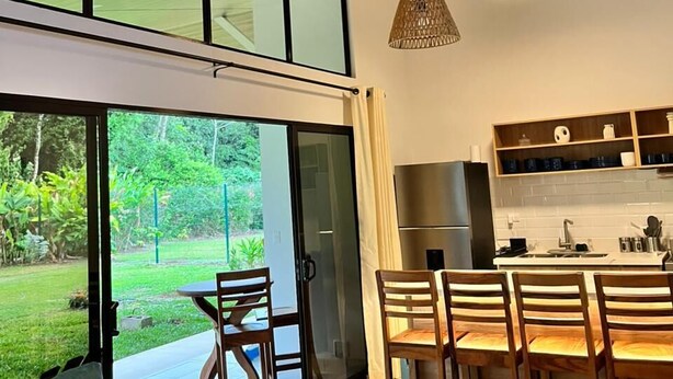 A modern kitchen with a dining area, large windows, and a ceiling fan.
