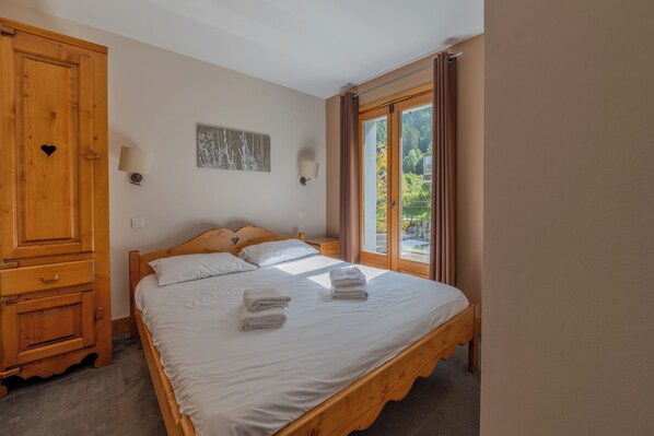 A bedroom with a wooden bed, two bedside tables, a wardrobe, and a window with curtains. - Vallorcine Balme 06 Ski In / Ski Out, Vallorcine (Argentiere), France (Vallorcine (Argentiere))