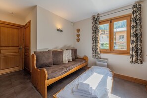 A room with a wooden bed, a sofa, a wardrobe, and a window with curtains. - Vallorcine Balme 06 Ski In / Ski Out, Vallorcine (Argentiere), France (Vallorcine (Argentiere))