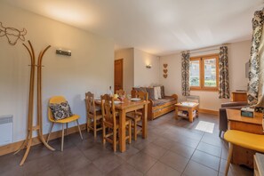 A dining area with a wooden table and chairs, a sofa, and a window with curtains. - Vallorcine Balme 06 Ski In / Ski Out, Vallorcine (Argentiere), France (Vallorcine (Argentiere))