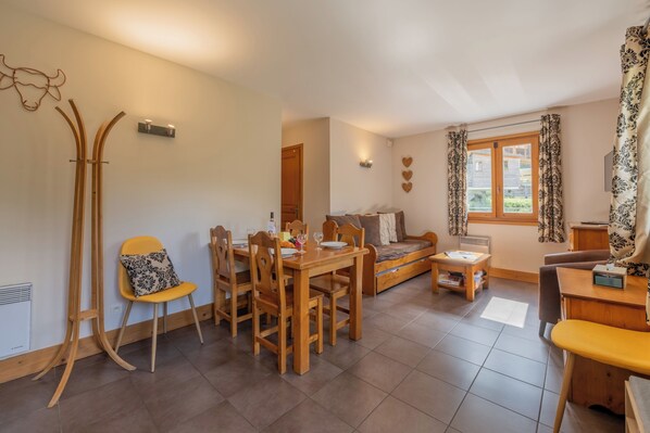 A dining area with a wooden table and chairs, a sofa, and a window with curtains. - Vallorcine Balme 06 Ski In / Ski Out, Vallorcine (Argentiere), France (Vallorcine (Argentiere))