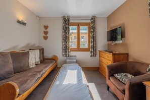 A room with a bed, a sofa, a wooden dresser, a television, and a window with curtains. - Vallorcine Balme 06 Ski In / Ski Out, Vallorcine (Argentiere), France (Vallorcine (Argentiere))