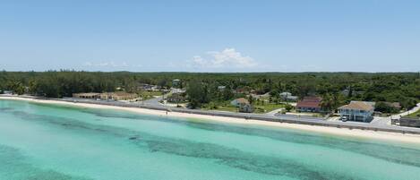 A coastal area with a beach, clear turquoise waters, and residential buildings.