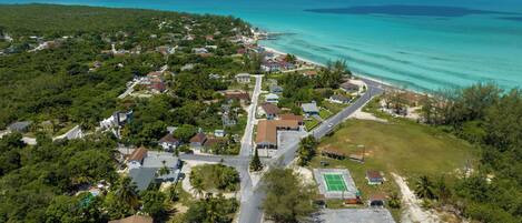 An aerial view of a coastal residential area with houses, a road, and a beach.