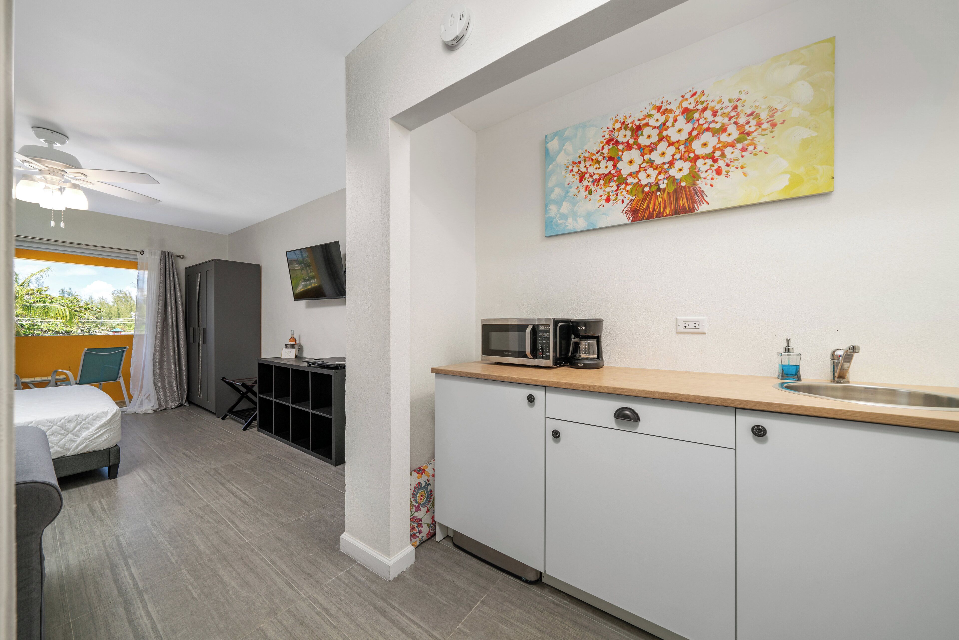 Une chambre d’hôtel compacte comprenant un coin cuisine, un lit, une télévision et une grande fenêtre avec des rideaux.