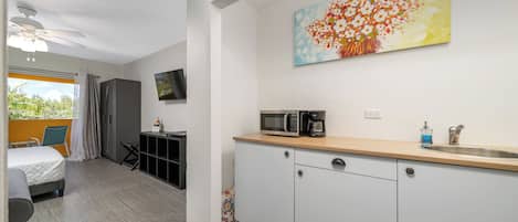 A compact hotel room with a kitchenette, a bed, a TV, and a large window with curtains.
