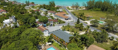 Ett flygbildsbild av ett bostadsområde vid kusten med hus, en swimmingpool och en strand.