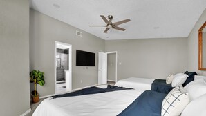 A bedroom with a bed, a ceiling fan, a TV, and a plant.