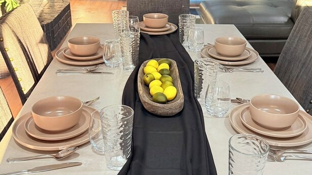 A dining table set with multiple plates, bowls, glasses, and cutlery, centered with a bowl of lemons.