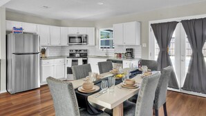 A modern kitchen with white cabinets, stainless steel appliances, and a dining area with grey upholstered chairs and a table set for four.