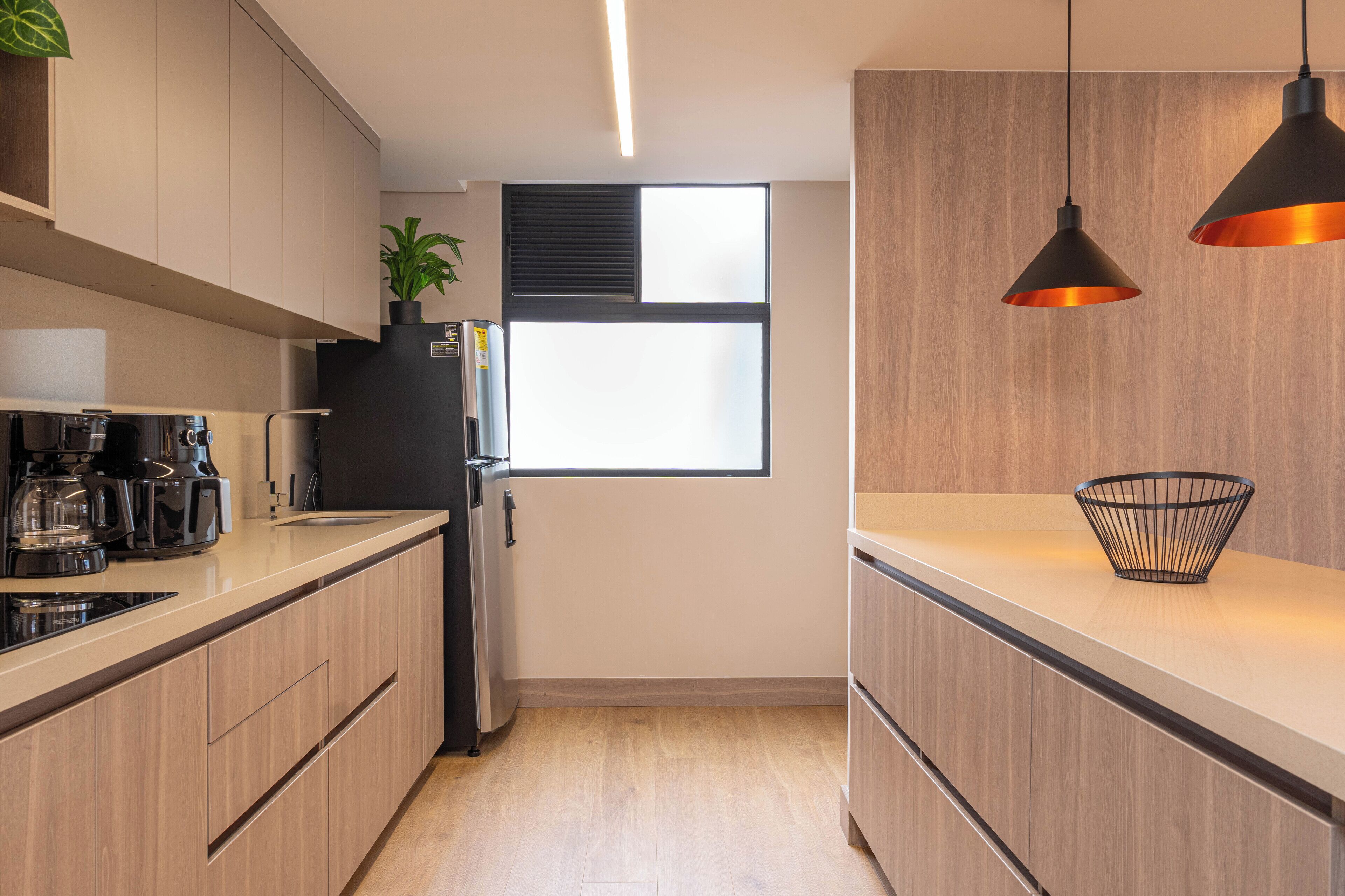 Een moderne keuken met houten kastjes, een inbouwoven, een koffiezetapparaat en hangende lampen.